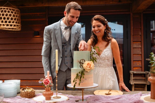 real bride sanneke – romantische A-lijn trouwjurk – bruid en bruidegom snijden samen een elegante bruidstaart aan; warme en blije uitstraling met zachte kleuren